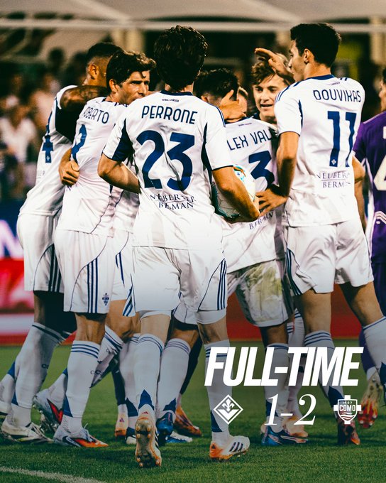 A group of soccer players in white jerseys with names like Perrone and Ouwerk on the backs, celebrating on a grassy field. The players are huddled together, wearing shorts and cleats, with some showing dirt on their uniforms. Text overlay reads "FULL-TIME 1-2".