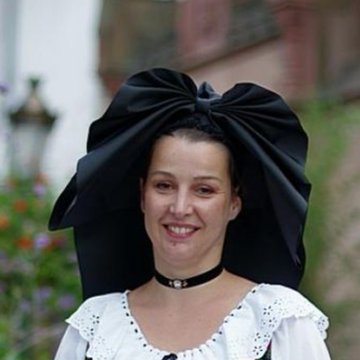 A woman wearing a large black bow hat and white lace-trimmed blouse, standing outdoors near a building with greenery. Another image shows a woman in a yellow headscarf and glasses, smiling, with text overlay reading "STRASBOURG LA DOUCEUR DE VILLE" and additional text including "Nocera, 64 ans.".