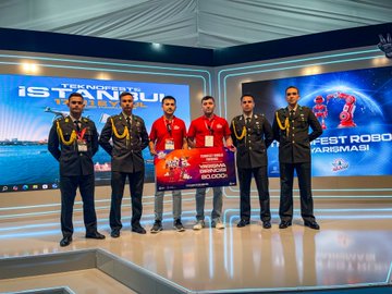 Three individuals in military uniforms holding award boxes, standing on a stage. A group of individuals in military uniforms posing together on a stage with a blue and white backdrop. Two people in casual attire holding a large check, flanked by individuals in military uniforms on a stage. Two individuals in business attire and military uniforms standing near a table with a sign labeled "INSPECTOR" and a screen displaying text.