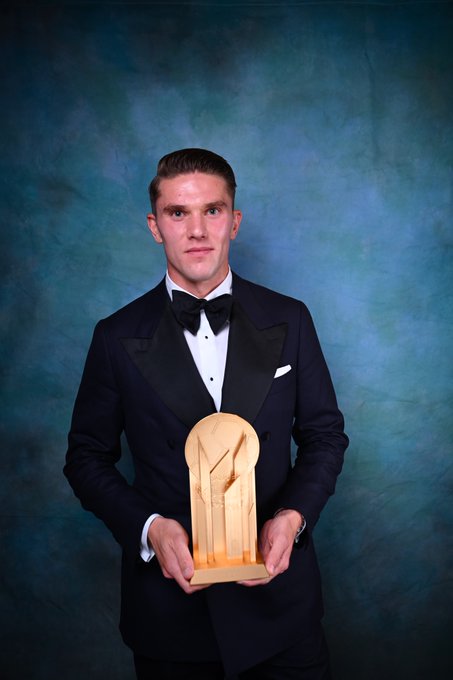 Viktor Gyökeres wearing a black tuxedo with a bow tie, holding a golden trophy with a unique design featuring abstract shapes.