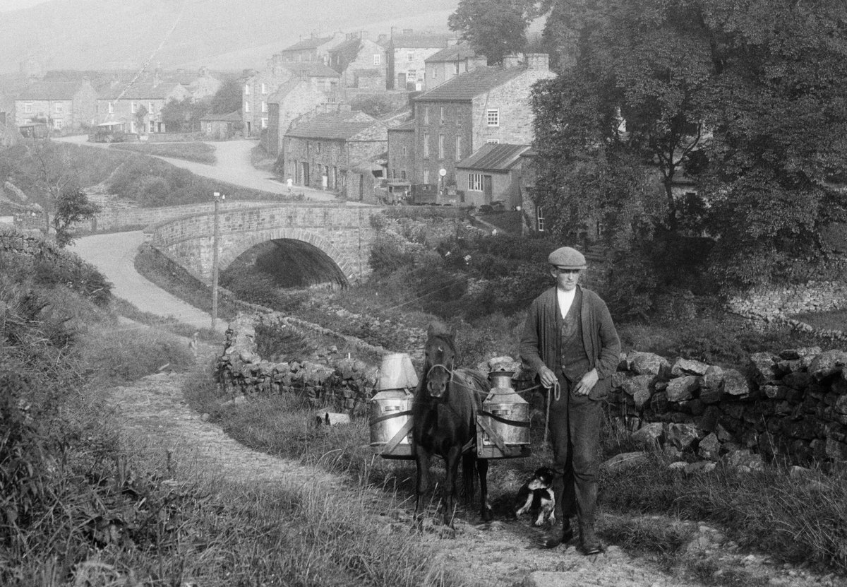 Taken in Muker, North Yorkshire, in 1930, this photograph captures the rural way of life. Milk churns, mule and flat cap. 🐎

Delivery lorries lurk in the background, hinting at a more mechanised future.