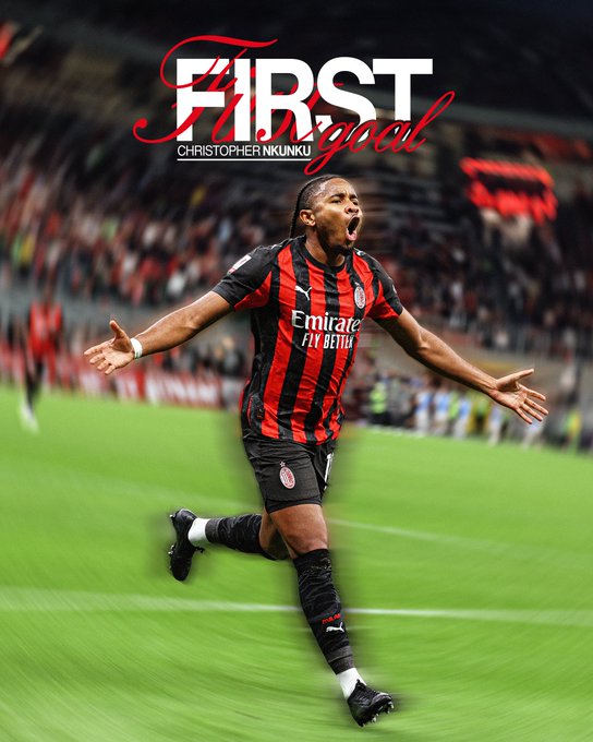 Christopher Nkunku running on a soccer field, wearing a black and red striped AC Milan jersey with "Emirates Fly Better" text. His arms are outstretched, and he appears to be celebrating. The background shows a stadium with a crowd and green grass.