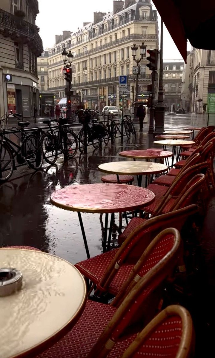 A rainy morning in Paris, the red chairs of a café patiently await the first customers under a gray sky