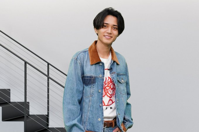 Ren Nagase wearing a denim jacket with brown corduroy collar over a white t-shirt with a red graphic, standing next to another person in a light blue t-shirt and dark pants. A third person in a denim jacket with brown corduroy collar over a white t-shirt with a red graphic and a beige cardigan stands beside them. A modern staircase with black railings and a white background are visible.