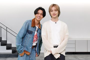 Ren Nagase wearing a denim jacket with brown corduroy collar over a white t-shirt with a red graphic, standing next to another person in a light blue t-shirt and dark pants. A third person in a denim jacket with brown corduroy collar over a white t-shirt with a red graphic and a beige cardigan stands beside them. A modern staircase with black railings and a white background are visible.