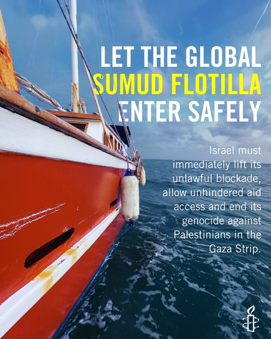 A red and white boat with a mast and rope, floating on blue water under a partly cloudy sky. Yellow text reads "LET THE GLOBAL SUMUD FLOTILLA ENTER SAFELY." White text below states "Israel must immediately lift its unlawful blockade, allow unhindered aid access and end its genocide against Palestinians in Gaza Strip." A logo is visible in the bottom right corner.