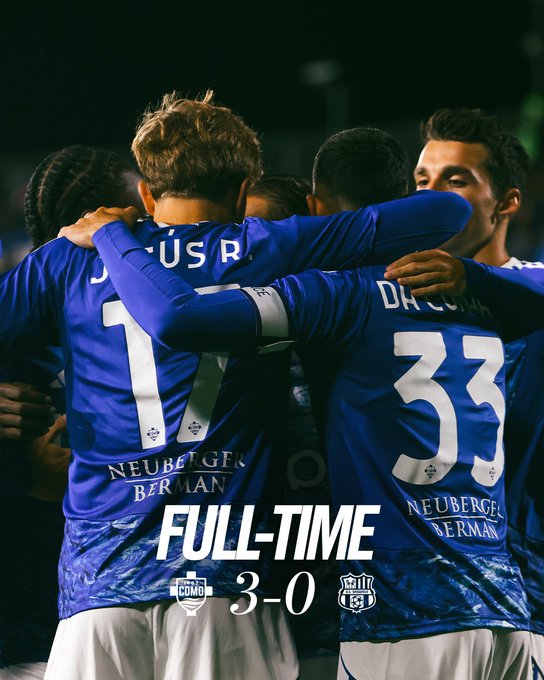 Players wearing blue jerseys with "NEUBERGER BERMAN" on the back, including one with "JESUS R" and number 17, and another with "DA COSTA" and number 33, standing together with arms around each other in a huddle. The text "FULL-TIME 3-0" is visible.