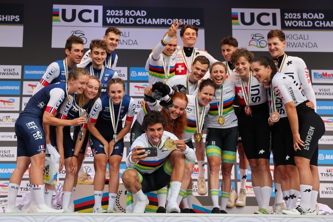 Cyclists wearing team uniforms stand on a podium, holding medals. Australia\'s team in rainbow jerseys stands at the center, France\'s team to their left, and Switzerland\'s team to their right. Banners display "UCI 2025 Road Championships" and "Kigali" with logos for sponsors like Shimano and Visit Rwanda.