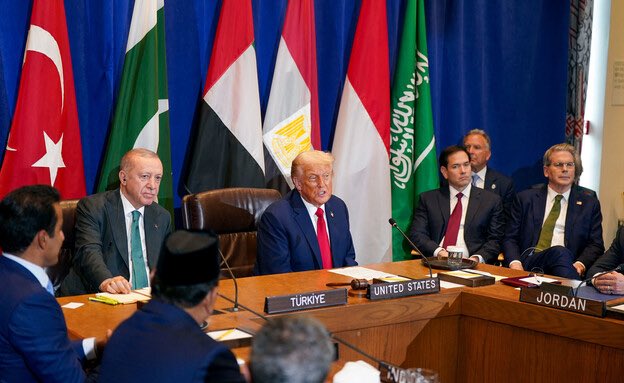 Donald Trump sitting at a conference table with nameplates reading 