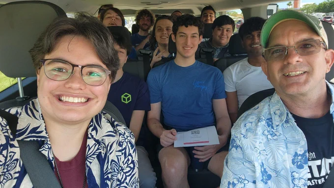 A group of people seated closely inside a vehicle, with one holding a piece of paper.