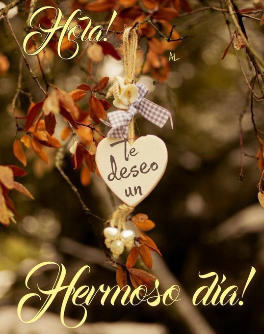 Autumn leaves in shades of orange and brown hang from tree branches. A heart-shaped ornament with the text "Te deseo un Hermoso día!" is suspended by a string with a bow. Yellow text reading "Hola!" and "Hermoso día!" is overlaid on the image.