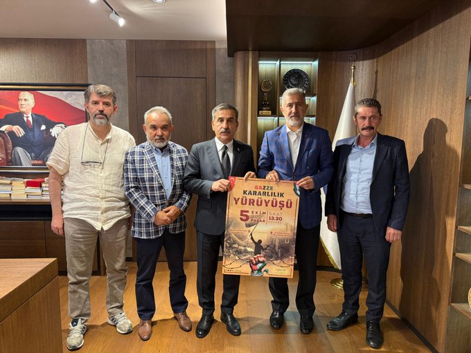 Five men standing in a wood-paneled room. İsmail Mansur Özdemir holds a poster with text reading "Gazze Kararlılık Yürüyüşü 5 Ekim 2023" and an illustration of a crowd. A large portrait of Mustafa Kemal Atatürk is on the wall behind them, along with a Turkish flag.