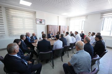 Students in white shirts and black pants holding Turkish flags, standing with a man in a suit. A large banner reads "Dr. Necip Öztürk Ortaokulu Açılış Töreni 28 Eylül 2023 / Adıyaman." A man in a suit speaks at a podium with microphones, flanked by Turkish flags and a banner featuring a portrait. People in suits and children sit at desks with flowers and balloons. Individuals in suits sit around a table in a meeting room.