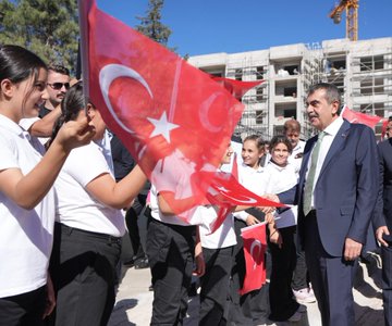 Students in white shirts and black pants holding Turkish flags, standing with a man in a suit. A large banner reads "Dr. Necip Öztürk Ortaokulu Açılış Töreni 28 Eylül 2023 / Adıyaman." A man in a suit speaks at a podium with microphones, flanked by Turkish flags and a banner featuring a portrait. People in suits and children sit at desks with flowers and balloons. Individuals in suits sit around a table in a meeting room.