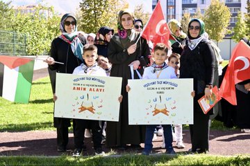 First image displays a large group of adults in formal suits and headscarves standing with young children in school uniforms holding certificates on a stage decorated with red balloons, lanterns, and a banner reading Malatya Muf tusu featuring Arabic script and event name Bed-i Besmele. Second image shows women in headscarves and children holding signs with Arabic text including Amin Alavi and event details, alongside Turkish and Palestinian flags in an outdoor grassy area. Third image captures a woman in abaya holding hands with several boys dressed in red fezzes and robes resembling Ottoman style, walking on grass with Turkish flags and smoke in background. Fourth image depicts a diverse crowd of adults and children, many in headscarves, gathered on grass near apartment buildings with Turkish and Palestinian flags.