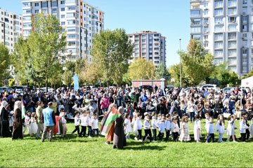 First image displays a large group of adults in formal suits and headscarves standing with young children in school uniforms holding certificates on a stage decorated with red balloons, lanterns, and a banner reading Malatya Muf tusu featuring Arabic script and event name Bed-i Besmele. Second image shows women in headscarves and children holding signs with Arabic text including Amin Alavi and event details, alongside Turkish and Palestinian flags in an outdoor grassy area. Third image captures a woman in abaya holding hands with several boys dressed in red fezzes and robes resembling Ottoman style, walking on grass with Turkish flags and smoke in background. Fourth image depicts a diverse crowd of adults and children, many in headscarves, gathered on grass near apartment buildings with Turkish and Palestinian flags.