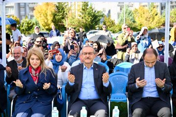First image shows a diverse group of people including men and women in formal attire and headscarves sitting on blue chairs under a canopy, engaged in prayer with hands raised, surrounded by autumn trees and umbrellas in an outdoor setting. Second image depicts a large crowd of attendees waving Turkish and Palestinian flags on a grassy field with tents and high-rise buildings in the background under a clear sky. Third image captures a man in a suit handing out striped gift bags to smiling children dressed in colorful outfits near balloons and trees. Fourth image features a group of suited officials and young girls in dresses holding medals on stage with a banner reading Malatya Müftülüğü Bed-i Besmele, decorated with green and red balloons.