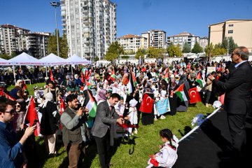 First image shows a diverse group of people including men and women in formal attire and headscarves sitting on blue chairs under a canopy, engaged in prayer with hands raised, surrounded by autumn trees and umbrellas in an outdoor setting. Second image depicts a large crowd of attendees waving Turkish and Palestinian flags on a grassy field with tents and high-rise buildings in the background under a clear sky. Third image captures a man in a suit handing out striped gift bags to smiling children dressed in colorful outfits near balloons and trees. Fourth image features a group of suited officials and young girls in dresses holding medals on stage with a banner reading Malatya Müftülüğü Bed-i Besmele, decorated with green and red balloons.
