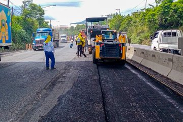 First image displays a gray truck and white milling machine on a road with barriers, workers in yellow vests operating yellow excavator near asphalt patches under cloudy sky. Second image shows blue and white milling machine with work zone sign on road flanked by trucks and workers in rain gear. Third image features workers in blue and yellow outfits around yellow Hyundai excavator spreading asphalt on road with traffic cones and vehicles nearby. Fourth image depicts workers near blue truck and yellow loader applying asphalt on road with barriers and greenery in background.
