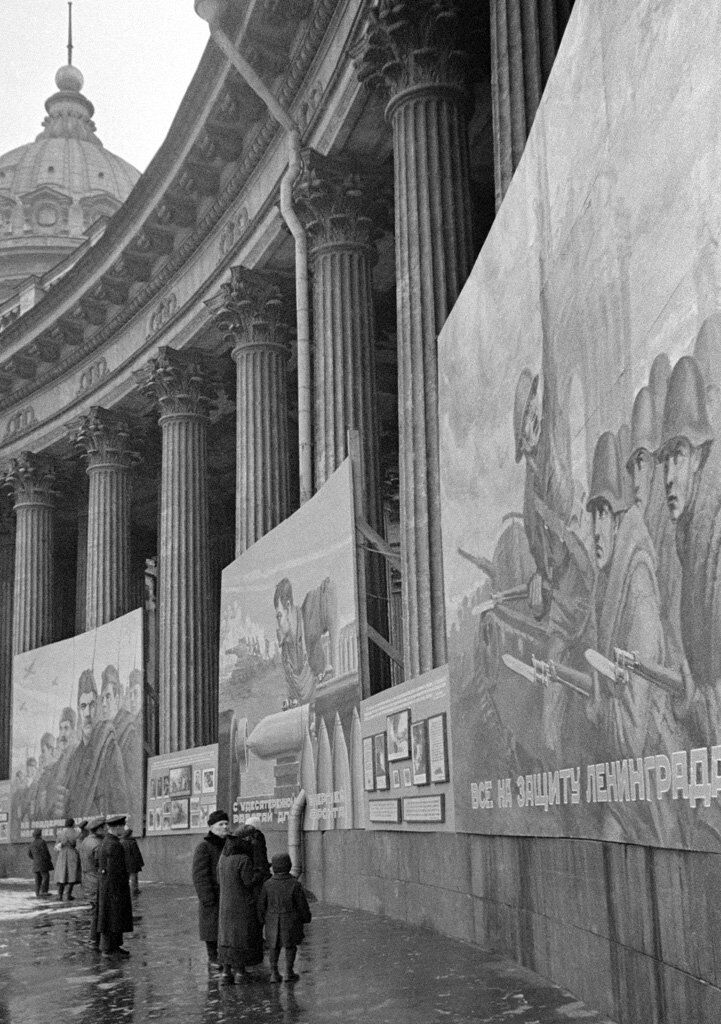 RealTimeWWII's tweet image. In besieged Leningrad, civilians congregate outside Kazan Cathedral, browsing Communist propaganda placards displayed on the pillars.