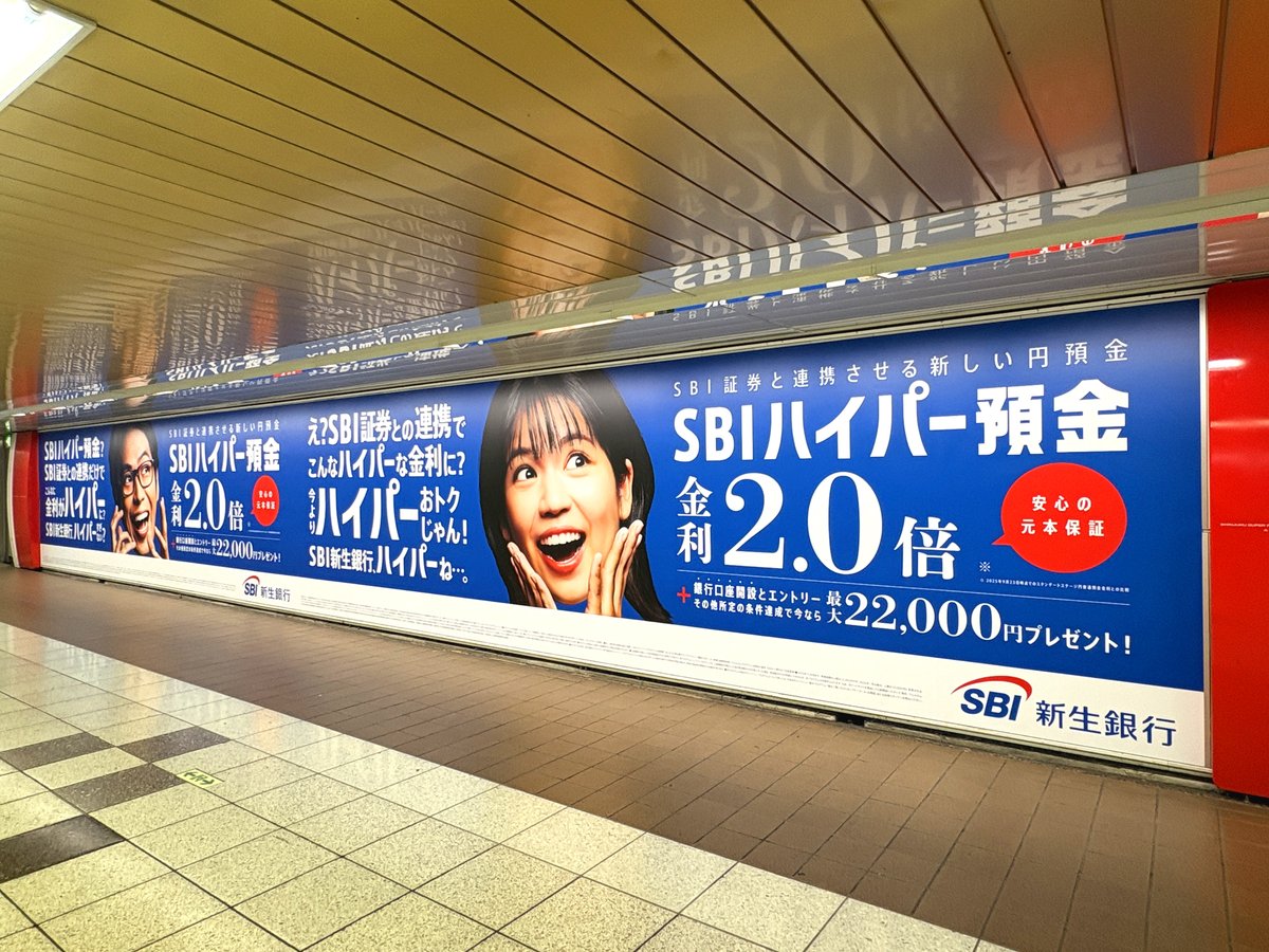 新宿メトロプロムナードに「SBIハイパー預金」の広告が展開中。特大シートと柱サイネージを使って、お得な情報を大きな文字＆笑顔のアップでアピールしています😀  乗り換えなどでこの通路を使う人にとっては、長い時間視界に入って印象付けされそうですね👀