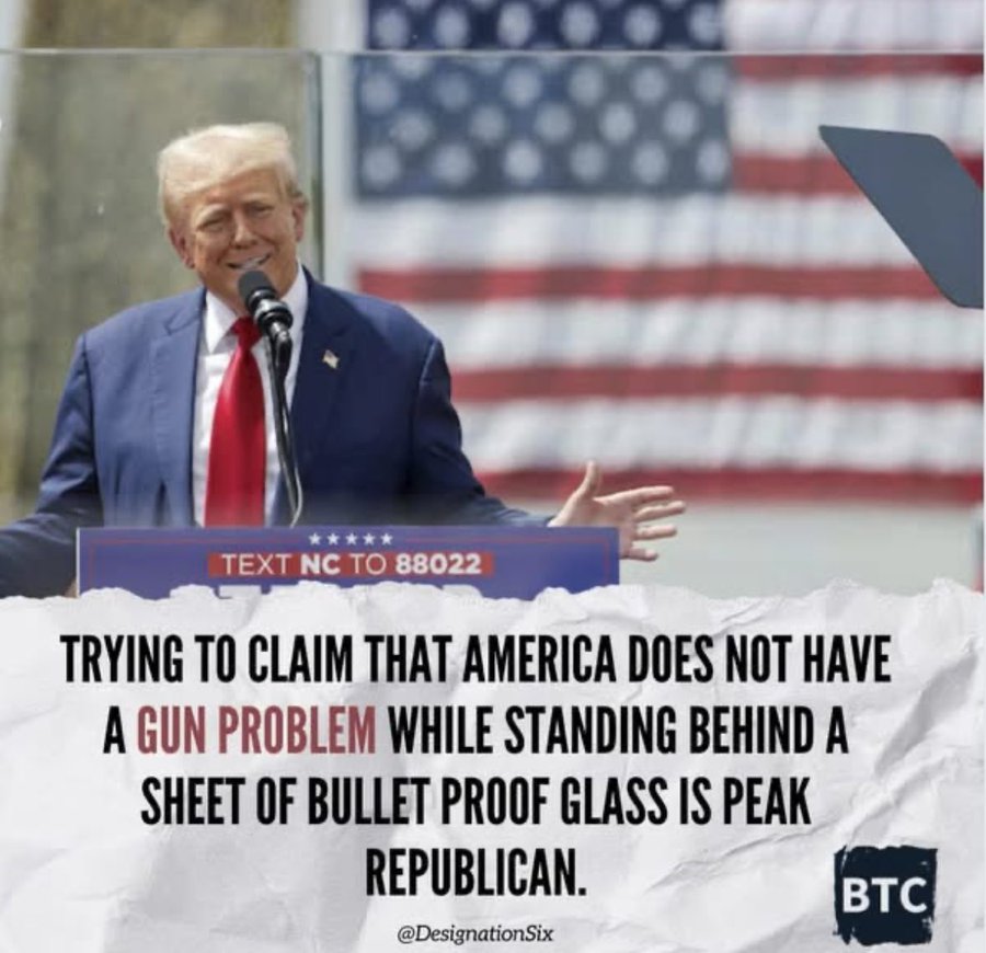 Donald Trump stands behind a podium with American flag backdrop, wearing blue suit and red tie, speaking into microphone with right hand raised, bulletproof glass panel in front, podium displays text to 80822, overlaid caption text reads Trying to claim that America does not have a gun problem while standing behind a sheet of bullet proof glass is peak Republican.