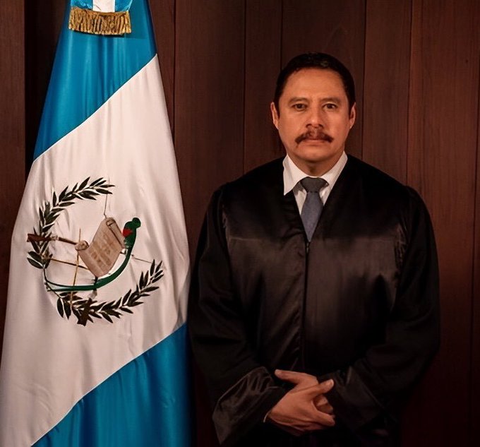 First image shows a man in black judicial robes and tie standing formally with hands clasped in front, beside a Guatemalan flag featuring blue and white vertical stripes with the national coat of arms in the center including a quetzal bird and scroll. Background is wooden paneling. Second image is an official document from the Constitutional Court of Guatemala dated October 9 2025 addressed to the Minister of Government detailing a complaint about an assassination attempt and requesting security measures with signatures and seals. Third image is another official Constitutional Court document signed by Rony Eulio LÃ³pez Contreras as substitute magistrate dated October 9 2025 requesting consideration of governmental measures and including a photo of the minister.