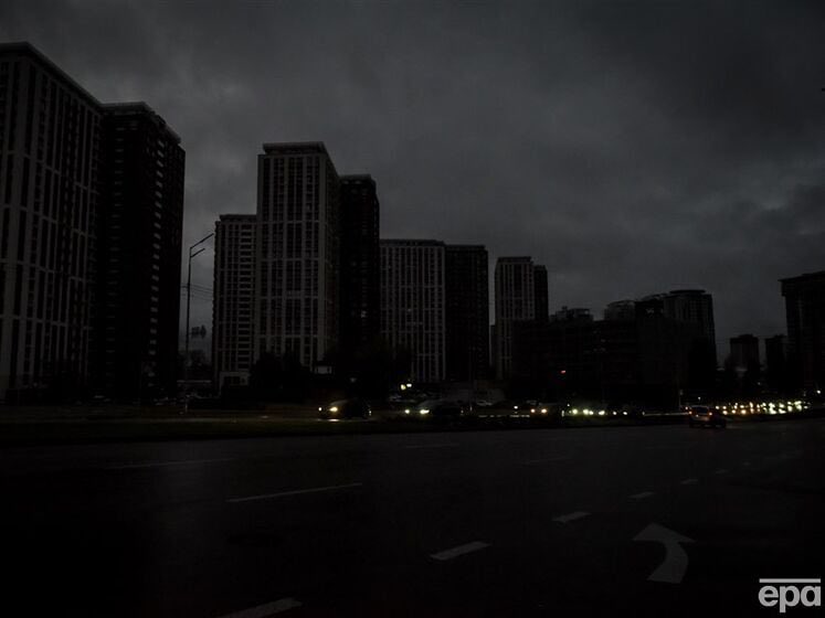 城市天际线的夜景，包括多栋高大的住宅和商业高层建筑，分散区域设有照明窗户。前景中有一条宽阔的多车道道路，有白色车道标记和指示方向的箭头。路灯和车辆前灯为道路沿线和附近区域提供最少的照明。天空阴沉，暗示着最近下雨或即将到来的天气，没有可见的人或其他物体。