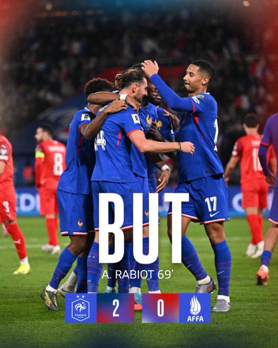 Group of male football players in blue France national team jerseys with numbers like 17 and 4 celebrate a goal by embracing and raising arms on a green soccer field during a match against Azerbaijan. In the background, more players in red and white kits stand on the pitch with stadium seating visible. Prominent text overlay reads BUT BUT in large white letters, A. RABIOT 69 below it, and score display shows France 2 - 0 Azerbaijan with French flag emblem and match logos.