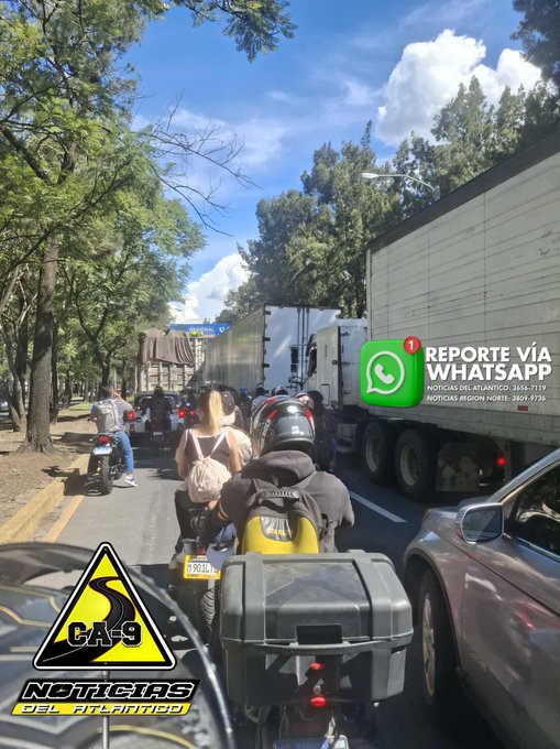 Primera imagen muestra una fila de vehÃ­culos detenidos en una carretera con Ã¡rboles a los lados bajo un cielo azul con nubes, incluyendo motos y autos en una congestiÃ³n causada por un accidente, con un trÃ¡iler grande visible al fondo y un logotipo de noticias en la esquina inferior derecha. Segunda imagen enfoca la parte trasera de un trÃ¡iler blanco con contenedor de carga, nÃºmeros de identificaciÃ³n como MNB004 y CS2094B visibles en el lado, marcas de Ã³xido y barro en la superficie, junto a una seÃ±al de advertencia amarilla de carretera y el mismo logotipo de noticias.