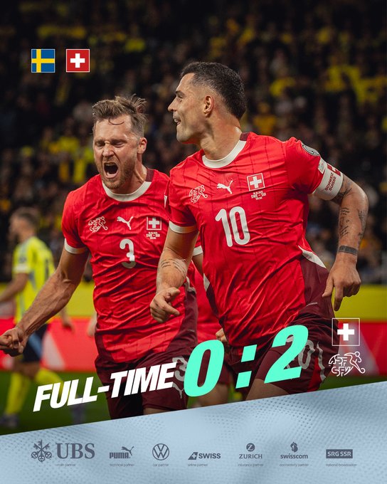 Two male football players in red Switzerland national team jerseys with numbers 3 and 10 stand side by side on a stadium field, one with short brown hair and the other with longer dark hair and beard, both smiling and embracing with arms around each other, yellow and blue Swedish flags visible in the blurred stadium crowd background, score overlay reads FULL-TIME 0:2 with Swiss cross emblem, sponsor logos including UBS Puma and Swiss at bottom.