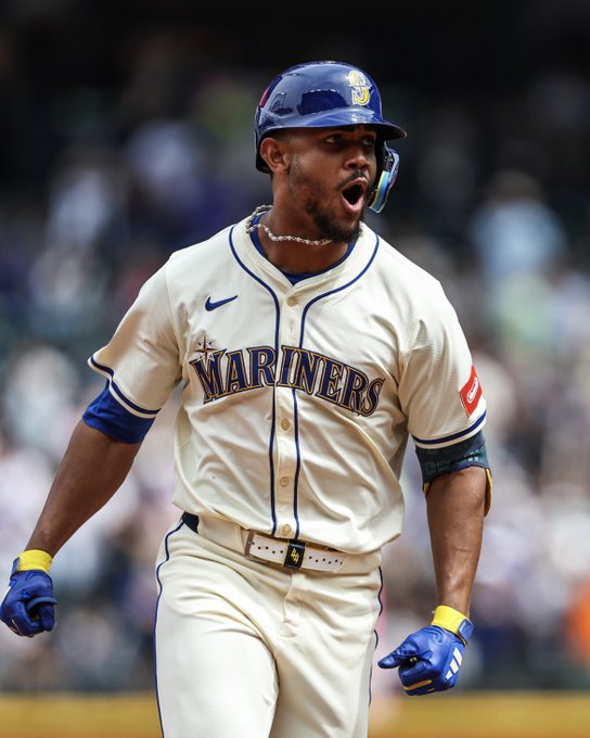 Julio Rodríguez yells in celebration. He wears a cream-colored Mariners alternate uniform and a blue helmet.