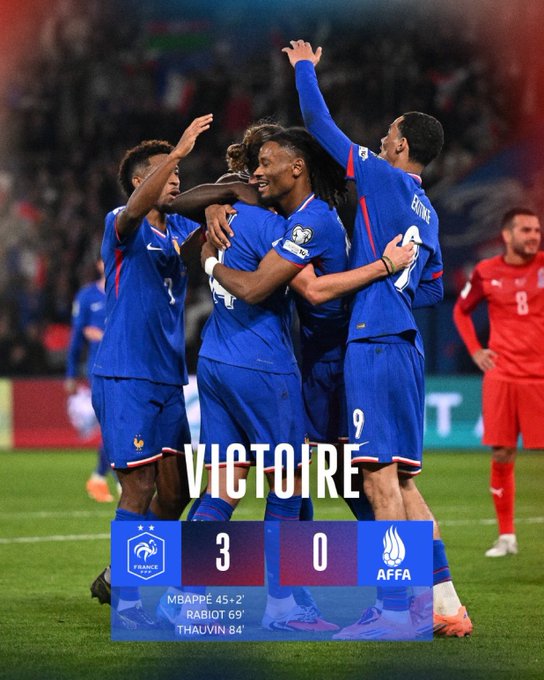 Group of male soccer players in blue France national team jerseys and shorts celebrate a victory by hugging and raising arms on a green stadium field at night under lights, with one player in a red referee jersey nearby, scoreboard overlay showing 3-0 win against Azerbaijan, French flag emblem visible.