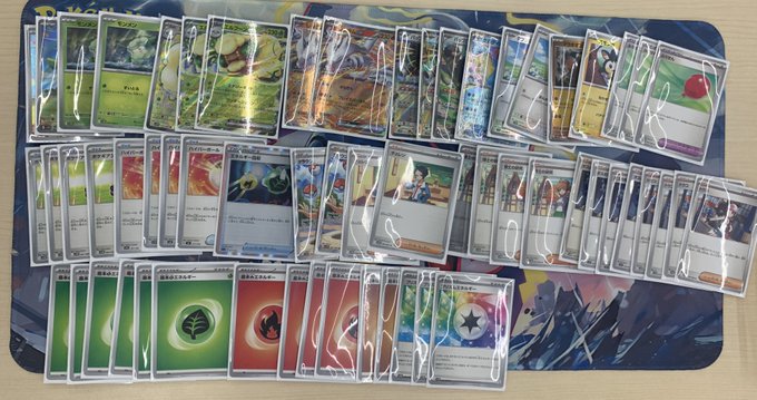 Assortment of colorful Pokemon trading card packs and individual cards arranged in rows on a blue play mat, featuring various artwork including green, yellow, red, and blue designs with fantasy creatures and symbols like leaves, flames, and stars, some cards sealed in clear wrappers.