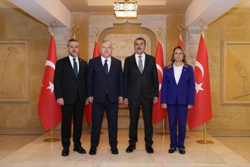 First image shows two men in dark suits standing at a wooden podium with Turkish flags on either side in a grand hall with ornate walls and lighting the podium labeled with gold text indicating governors office. Second image depicts four individuals two men and two women in formal suits and blazers posing together in front of Turkish flags in a similar ornate hall with geometric wall designs. Third image features a group of eight people including men and women in business attire seated around a wooden table with plants and water glasses in a room with wooden paneling and more Turkish flags.