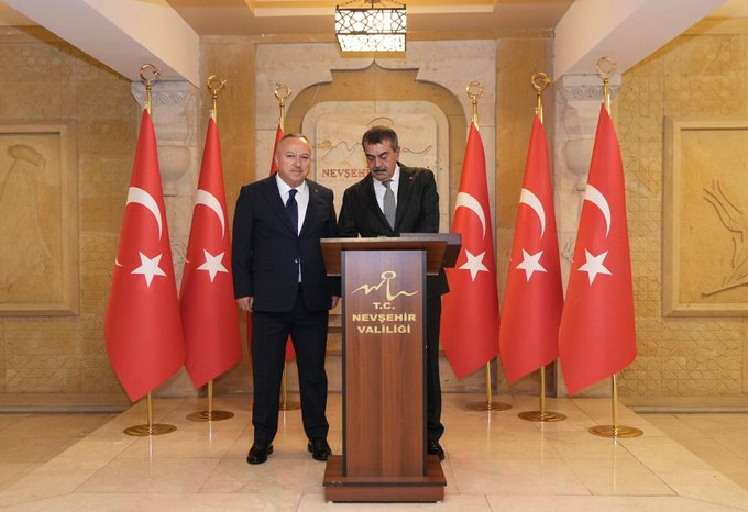 First image shows two men in dark suits standing at a wooden podium with Turkish flags on either side in a grand hall with ornate walls and lighting the podium labeled with gold text indicating governors office. Second image depicts four individuals two men and two women in formal suits and blazers posing together in front of Turkish flags in a similar ornate hall with geometric wall designs. Third image features a group of eight people including men and women in business attire seated around a wooden table with plants and water glasses in a room with wooden paneling and more Turkish flags.