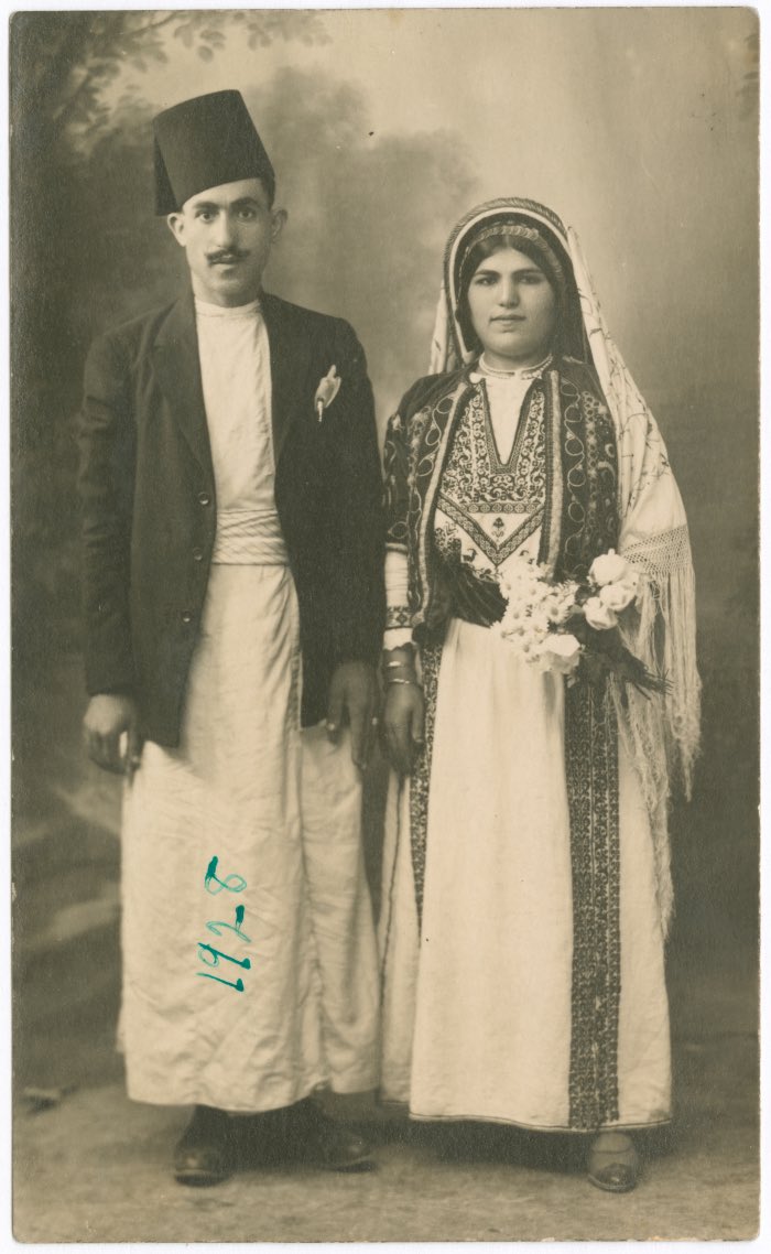 October 20th, 1920, Ramallah, Palestine 🇵🇸 

Boutros Issa Al-Abd and his wife, Shafa Khalil Al-Khoury. 

Al-Abd is seen standing, wearing a tarboush (fez), a traditional robe (qumbaz), and a belt, while Al-Khoury stands beside him dressed in a traditional Palestinian thobe from