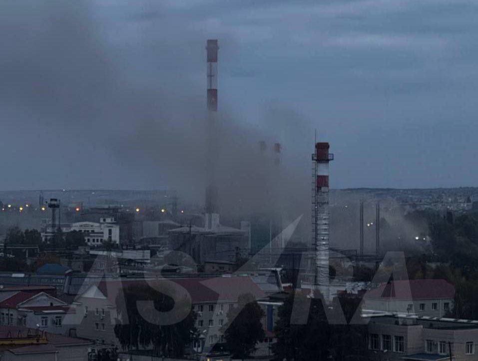 工业区的照片，有多个烟囱冒烟。在多云的天空中，可以看到两个高大的烟囱，一个有红白条纹。背景中可以看到建筑物和电线，图像上有一个水印，上面写着“ASARA”。