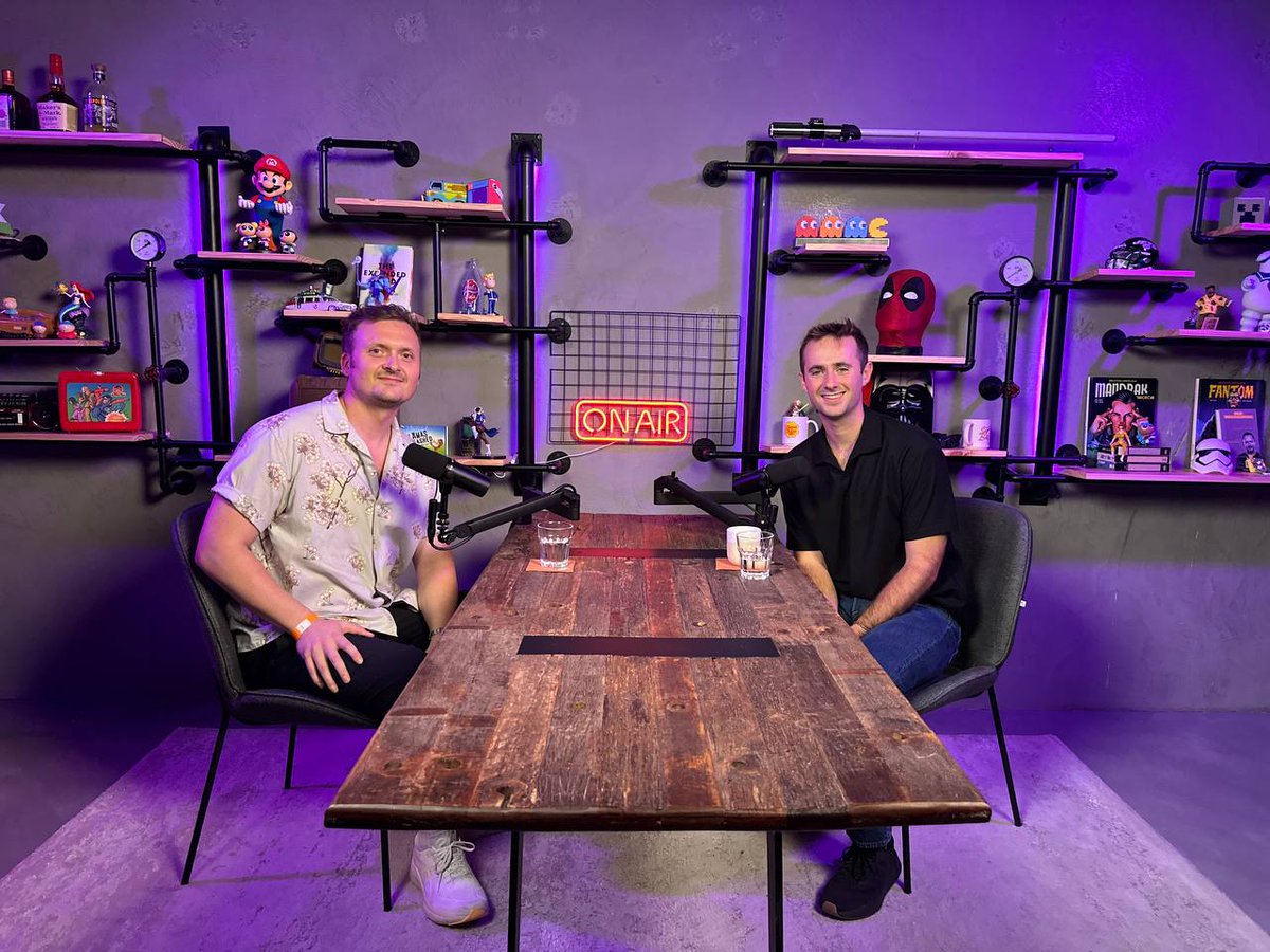 Robbie Rollup 和 ASvanevik 在充满极客风格装饰并带有“ON AIR”标志的活力播客录音室中