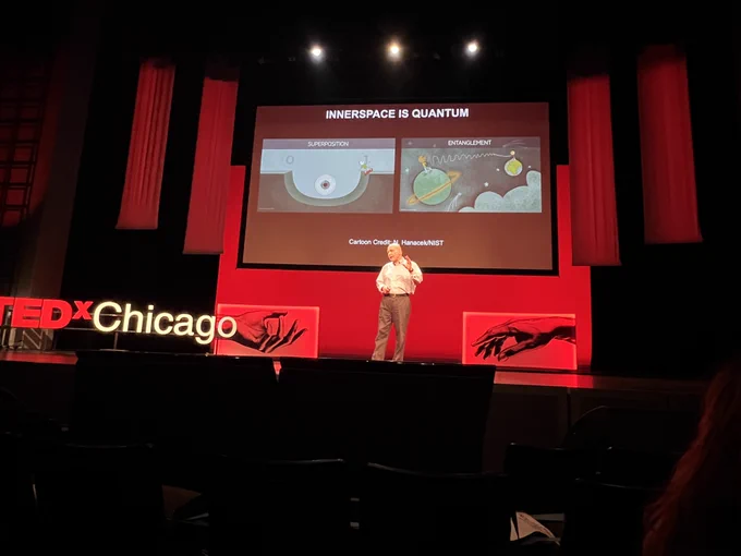 David Awschalom stands on TEDx stage in front of screen displaying two graphics - one on superposition and one on entanglement