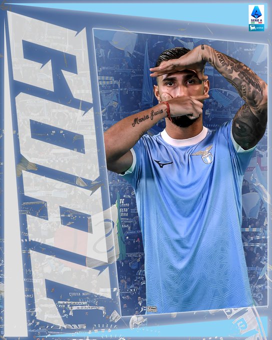 Taty Castellanos wearing a light blue Lazio soccer jersey with tattoos on his arms, including "Mamma Mia" on one arm. He is making a gesture with both hands near his face. The background features a digital pattern in blue and white with the word "GOAL" repeated.