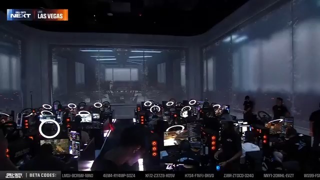 A crowded gaming tournament stage in Las Vegas with multiple PC setups featuring ring lights and gaming PCs; on-screen text reads 'NEXT LAS VEGAS' and 'BETA CODES' along with various codes.