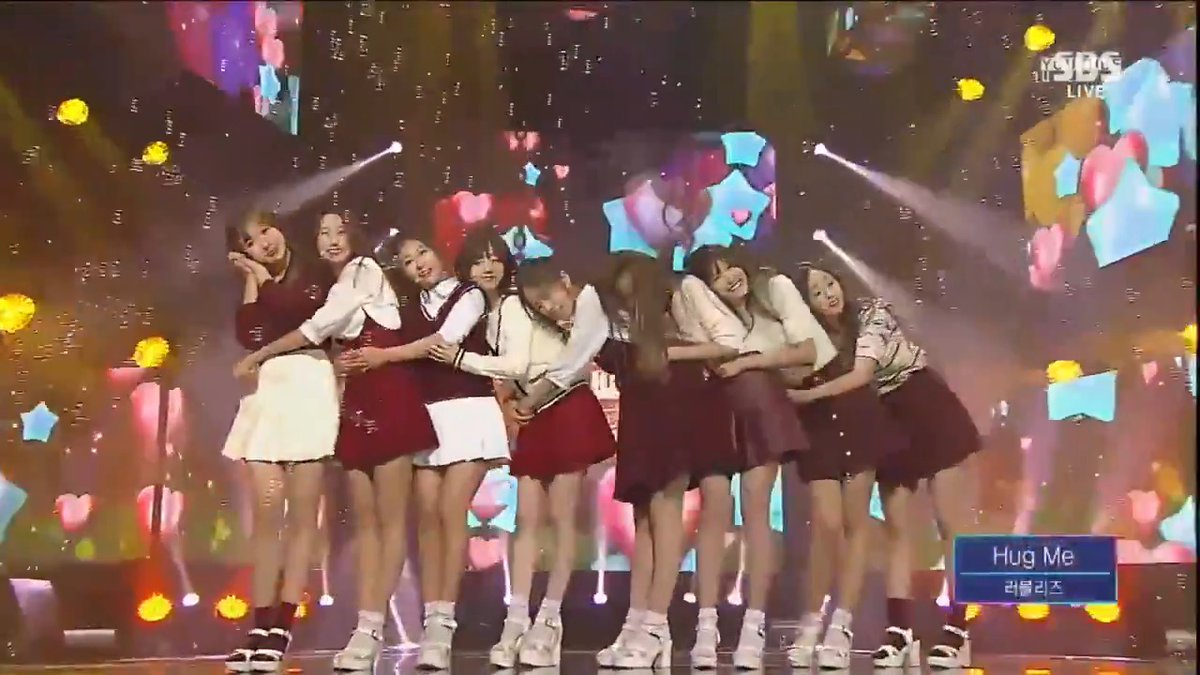 A K-pop girl group performance on stage with members in school uniform-style outfits, with text on screen reading 'Hug Me' and '러블리즈' (Lovelyz), and 'LIVE' and 'SBS' logos visible.