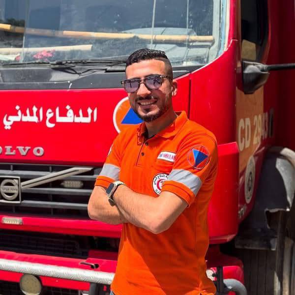 Munthir Raed AlDahshan stands in front of a red Volvo fire truck. He wears an orange polo shirt with a Civil Defense logo and reflective arm bands. Arabic text on the truck reads "الإنقاذ المدني" (Civil Defense) and "CD 240".