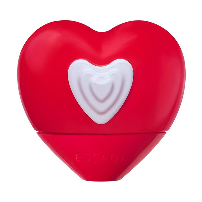 A red heart-shaped perfume bottle with a white heart design on the front. The bottle has the name "ESCADA" visible at the bottom. The design is sleek and glossy.