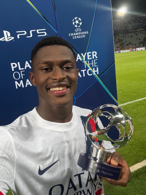 Nuno Mendes wearing a white Paris Saint-Germain jersey with a Nike logo and Qatar Airways text, holding a UEFA Champions League Player of the Match trophy. He stands on a soccer field with a blue backdrop displaying the UEFA Champions League logo and PlayStation 5 branding.