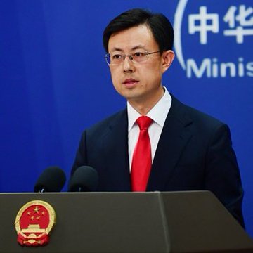 A man in a dark suit and red tie stands at a podium with microphones, wearing glasses. The podium bears a red emblem with a gold design. Behind him is a blue background with the Chinese characters for "Ministry" and the English word "Minis" partially visible. A world map below shows flags and numbers indicating 497 participants from 46 countries.