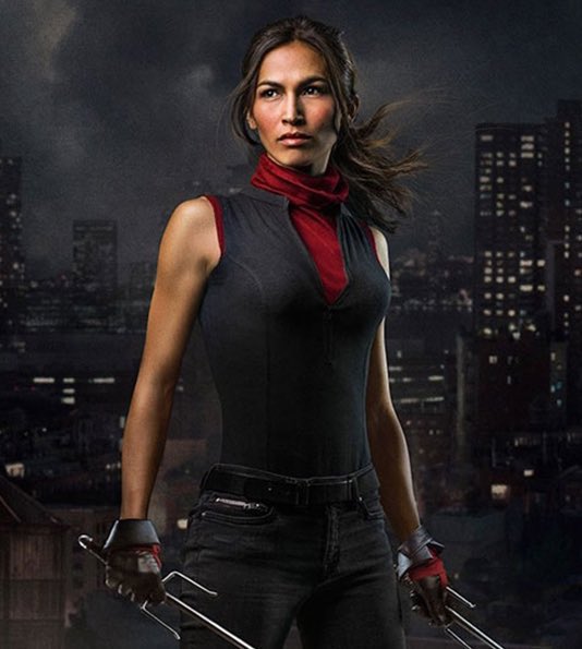 Elektra Natchios wearing a black sleeveless top, red scarf, black gloves, and holding sai weapons. She stands against a city skyline background at night. The text "MARVEL TELEVISION DAREDEVIL BORN AGAIN" is visible below.