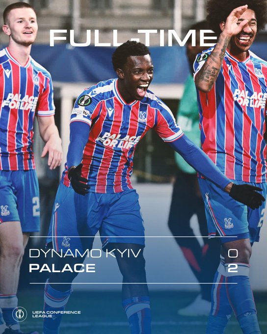Three Crystal Palace soccer players in red and blue striped jerseys with "Palace For Life" text, celebrating on a field. One player in the center is smiling broadly, arms raised, wearing blue shorts and black gloves. The text overlay reads "FULL TIME," "DYNAMO KYIV 0," "CRYSTAL PALACE 2," and "UEFA CONFERENCE LEAGUE."