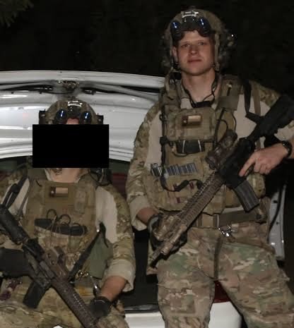 Two individuals in military gear, including helmets with night vision goggles, tactical vests, and camouflage uniforms. They are holding rifles and standing in front of a white vehicle at night. One individual is identified as Greg Stoker, a former Army Ranger, based on the post text.